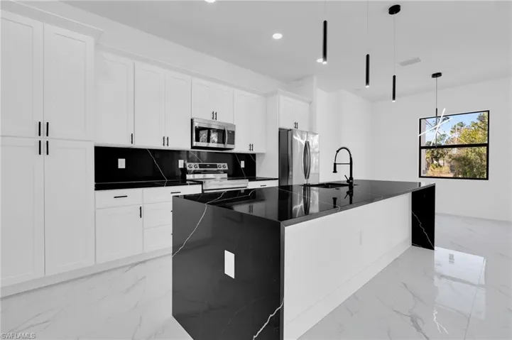 Kitchen with a kitchen island with sink, appliances with stainless steel finishes, hanging light fixtures, white cabinets, and decorative backsplash