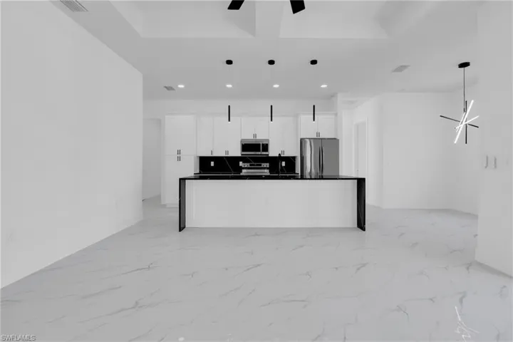Kitchen with stainless steel appliances, white cabinetry, light marble finish floors, a spacious island, and decorative light fixtures