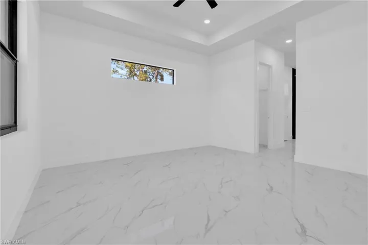 Unfurnished room featuring a raised ceiling, light marble finish flooring, recessed lighting, and a ceiling fan