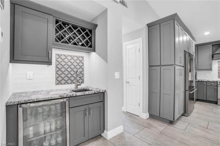 Kitchen featuring high end fridge, gray cabinets, tasteful backsplash, light stone countertops, and wine cooler