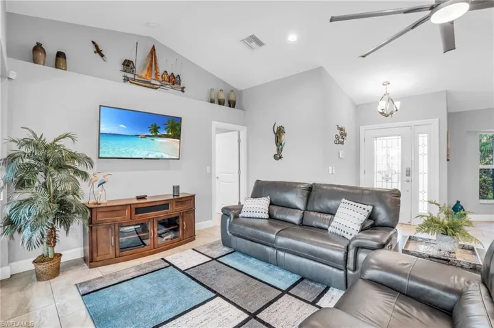 Tiled living room featuring high vaulted ceiling and ceiling fan with notable chandelier