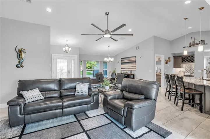 Tiled living room with sink, ceiling fan with notable chandelier, and lofted ceiling