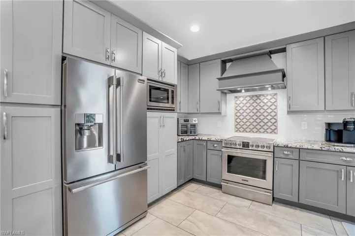 Kitchen with tasteful backsplash, light tile patterned floors, light stone counters, custom exhaust hood, and high quality appliances