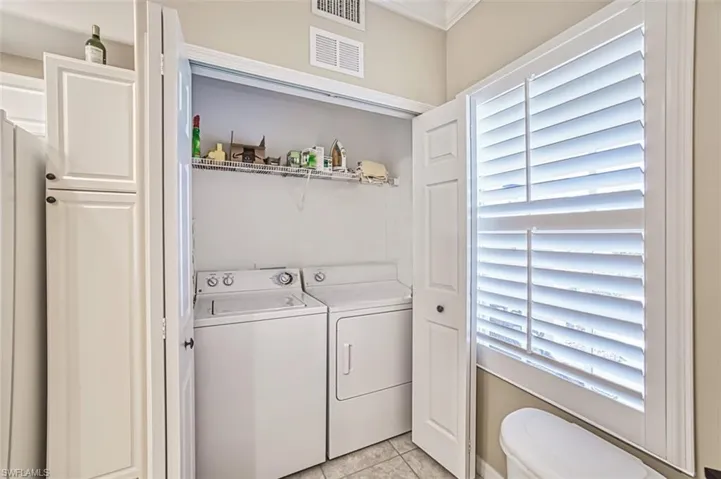 Laundry area with light tile patterned flooring, washing machine and dryer, ornamental molding, and plenty of natural light