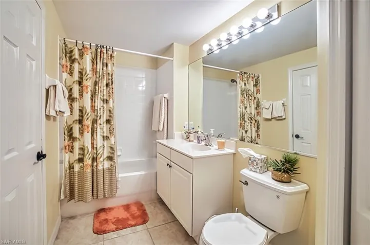 Full bathroom with tile patterned floors, shower / bathtub combination with curtain, toilet, and vanity