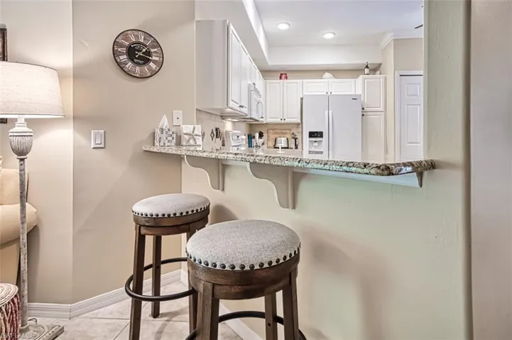 Kitchen featuring white cabinetry, tasteful backsplash, white appliances, light tile patterned floors, and a kitchen breakfast bar