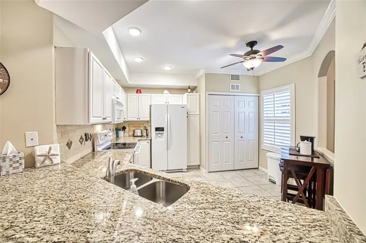 Kitchen with light tile patterned flooring, white appliances, backsplash, ceiling fan, and sink
