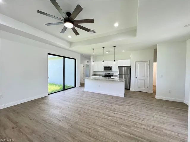 Unfurnished living room with light hardwood / wood-style flooring, ceiling fan, and a tray ceiling