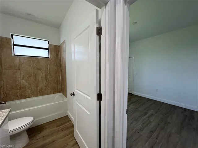 Full bathroom with vanity, hardwood / wood-style flooring, tiled shower / bath, and toilet