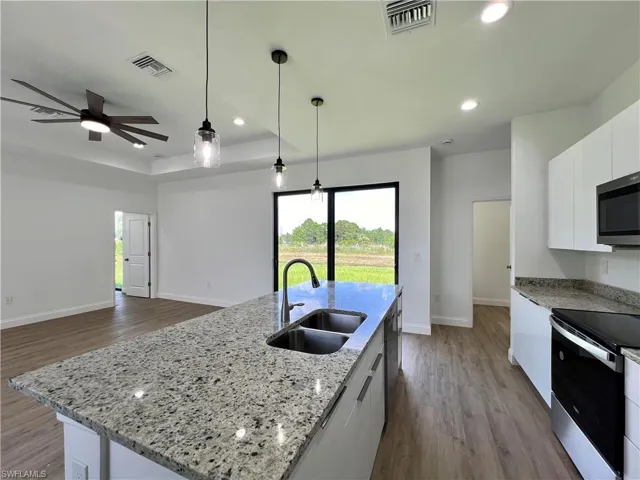 Kitchen with appliances with stainless steel finishes, sink, a kitchen island with sink, and white cabinets