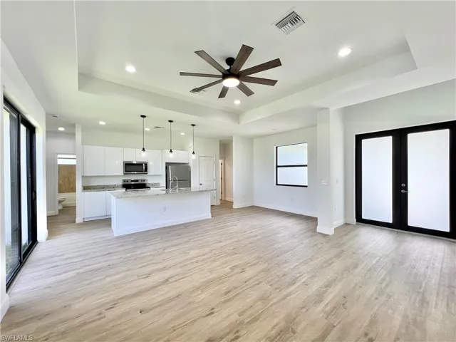 Kitchen with decorative light fixtures, white cabinetry, a raised ceiling, appliances with stainless steel finishes, and light hardwood / wood-style flooring