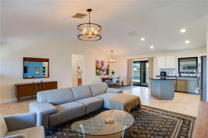 Living room with light tile patterned floors, suspended lighting, and lofted ceiling