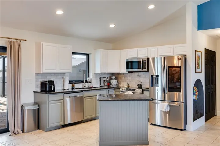 Kitchen with stainless steel appliances, lofted ceiling, dark stone counters, tasteful backsplash, and light tile patterned floors