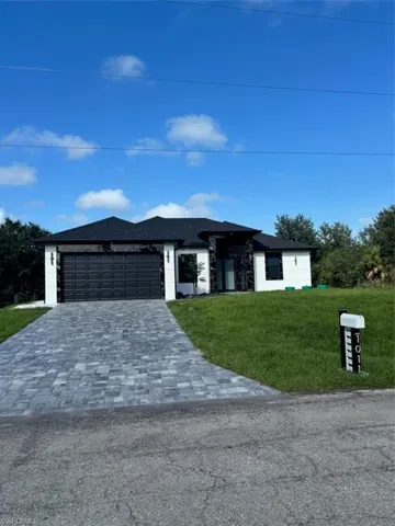 Prairie-style home featuring a front lawn, decorative driveway, an attached garage, and roof with shingles