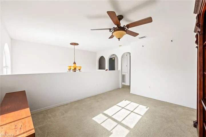 Empty room with a chandelier, light carpet, and a ceiling fan