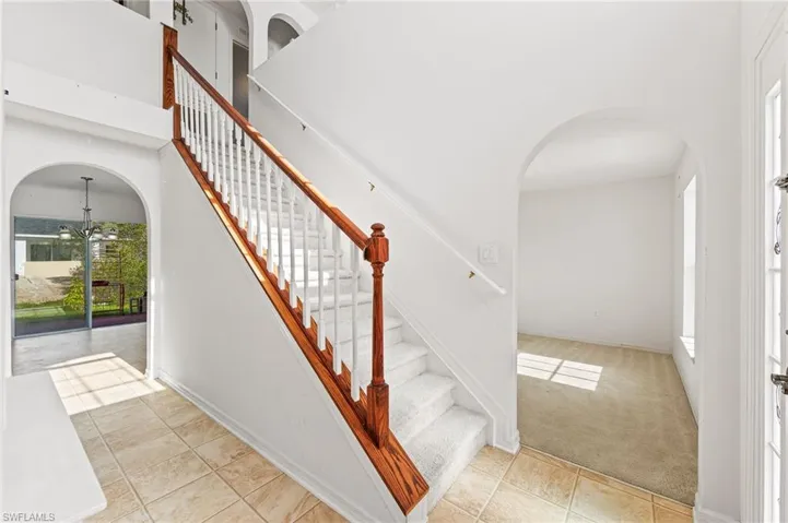 Stairway featuring arched walkways, a chandelier, tile patterned floors, carpet, and a towering ceiling
