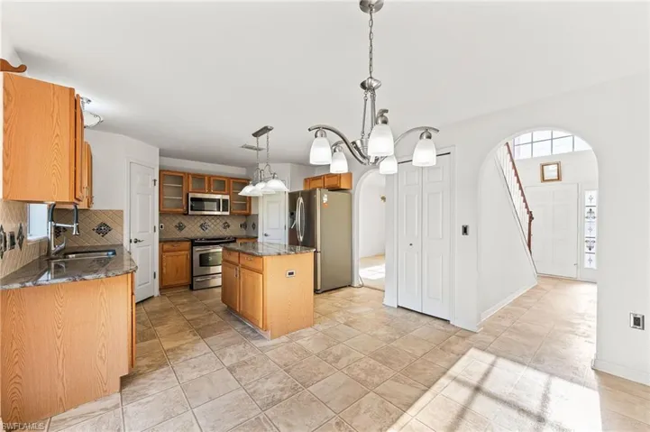 Kitchen with stainless steel appliances, arched walkways, a center island, backsplash, and glass insert cabinets