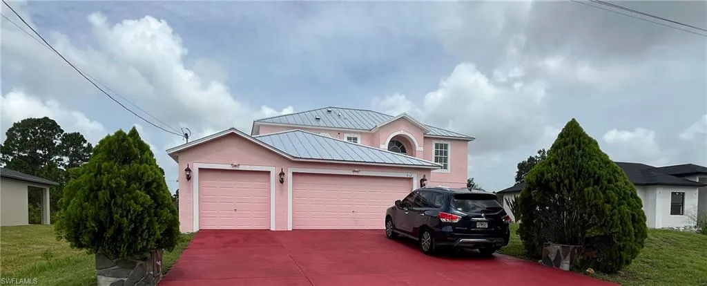 Traditional-style house with stucco siding, a standing seam roof, an attached garage, and driveway