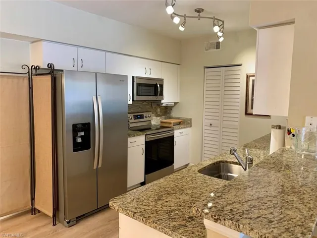 Kitchen with appliances with stainless steel finishes, light stone countertops, white cabinets, tasteful backsplash, and a peninsula