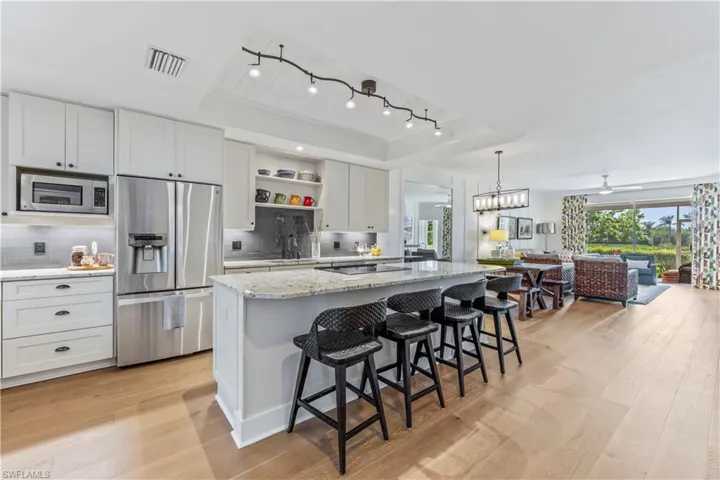 Kitchen through living with light wood-flooring,  kitchen island with sink, backsplash, and track lighting