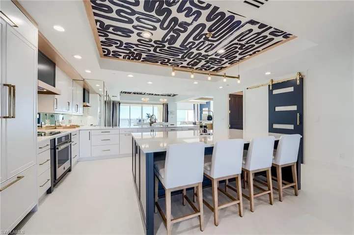 Kitchen with a raised ceiling, a barn door, white cabinetry, a kitchen bar, and light countertops