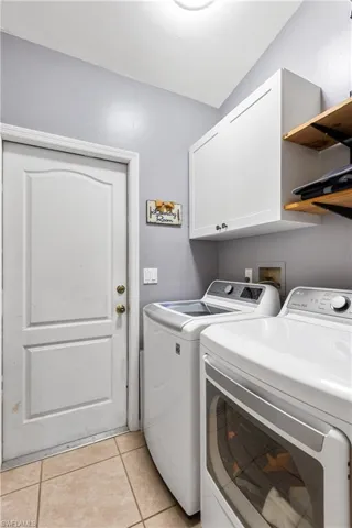 Clothes washing area featuring light tile patterned floors, washer and clothes dryer, and cabinets