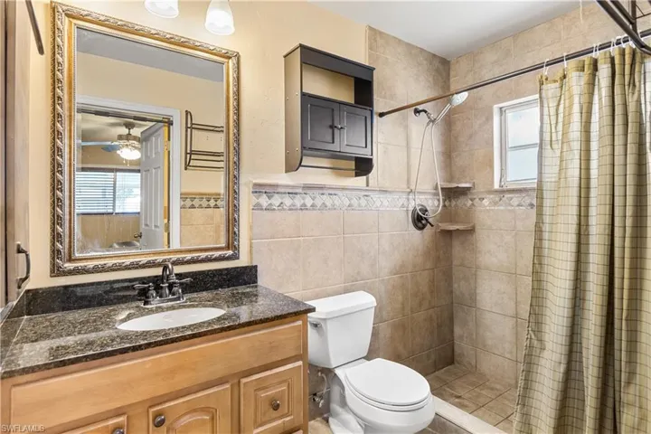 Bathroom featuring toilet, vanity, ceiling fan, tile walls, and curtained shower