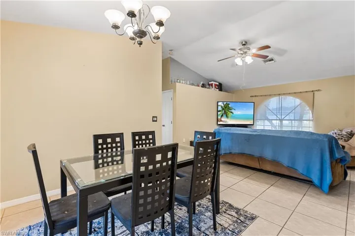 Tiled dining room with ceiling fan with notable chandelier and vaulted ceiling