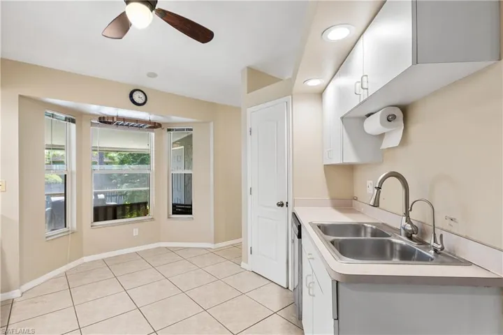 Kitchen with light tile patterned floors, white cabinets, dishwasher, ceiling fan, and sink