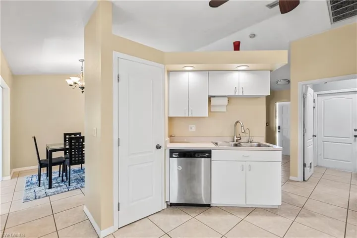 Kitchen featuring white cabinetry, ceiling fan with notable chandelier, light tile patterned floors, and stainless steel dishwasher