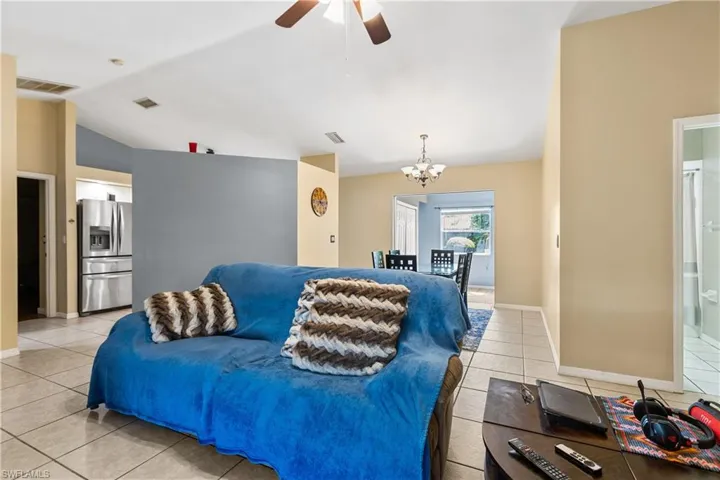 Tiled living room with lofted ceiling and ceiling fan with notable chandelier