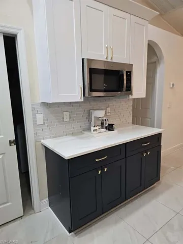 Kitchen with white cabinetry, dark cabinets, stainless steel microwave, arched walkways, and decorative backsplash