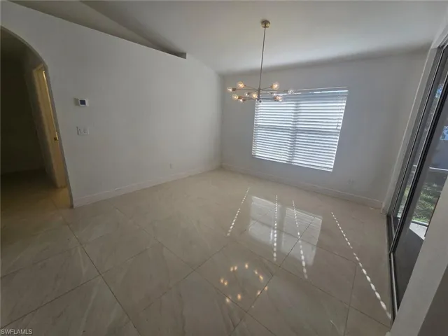 Unfurnished dining area featuring lofted ceiling, arched walkways, a chandelier, and light tile patterned floors