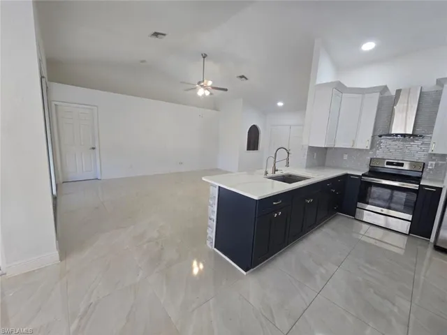 Kitchen featuring dark cabinets, electric stove, white cabinets, wall chimney exhaust hood, and light stone countertops