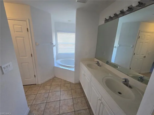 Full bathroom featuring double vanity, light tile patterned floors, and a bath