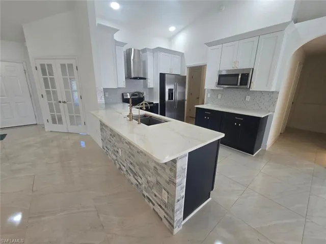 Kitchen featuring white cabinets, dark cabinets, french doors, light stone countertops, and arched walkways