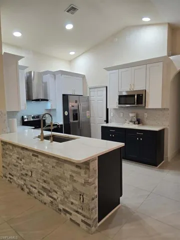 Kitchen with lofted ceiling, decorative backsplash, a peninsula, appliances with stainless steel finishes, and wall chimney exhaust hood