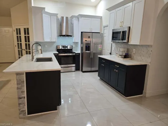 Kitchen with white cabinets, stainless steel appliances, decorative backsplash, wall chimney exhaust hood, and dark cabinets