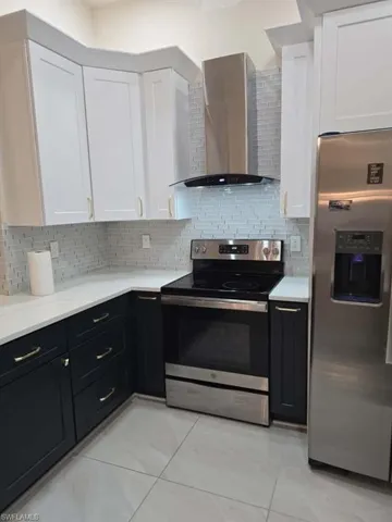 Kitchen with dark cabinets, stainless steel appliances, white cabinets, wall chimney range hood, and backsplash
