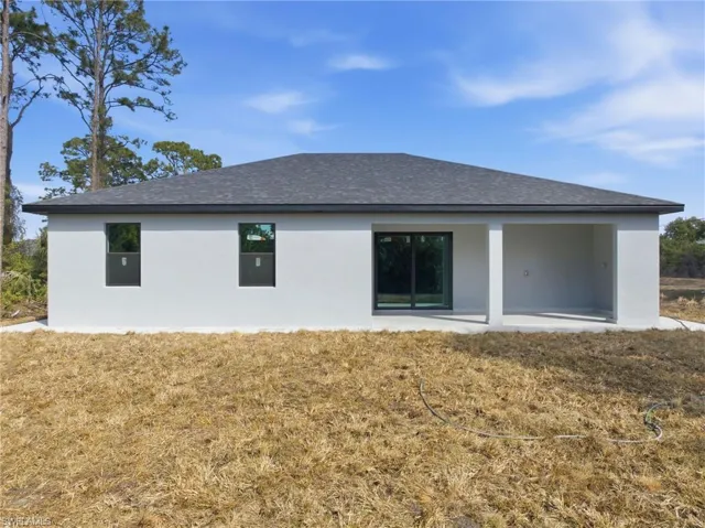 Rear view of property featuring a lawn and stucco siding