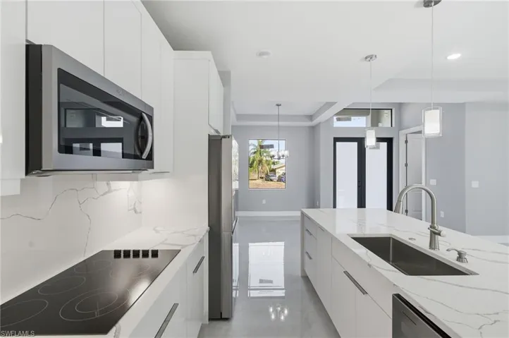 Kitchen with modern cabinets, stainless steel appliances, white cabinetry, light stone counters, and a raised ceiling
