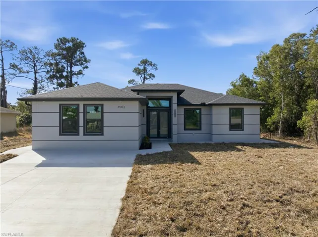 Prairie-style home with a shingled roof, driveway, and a front lawn