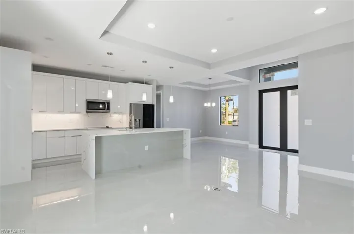 Kitchen featuring white cabinetry, an island with sink, stainless steel appliances, a tray ceiling, and modern cabinets