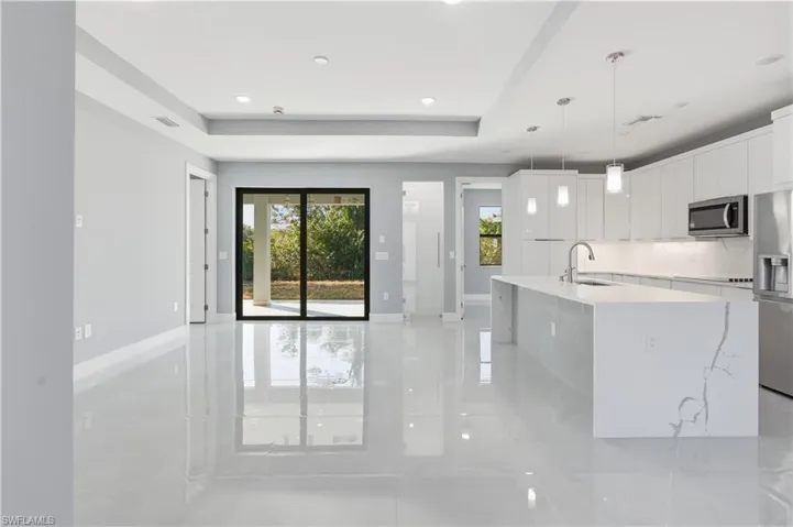 Kitchen with a raised ceiling, white cabinetry, stainless steel appliances, a kitchen island with sink, and light stone countertops
