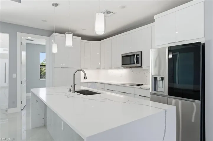 Kitchen featuring stainless steel appliances, modern cabinets, white cabinets, a center island with sink, and pendant lighting