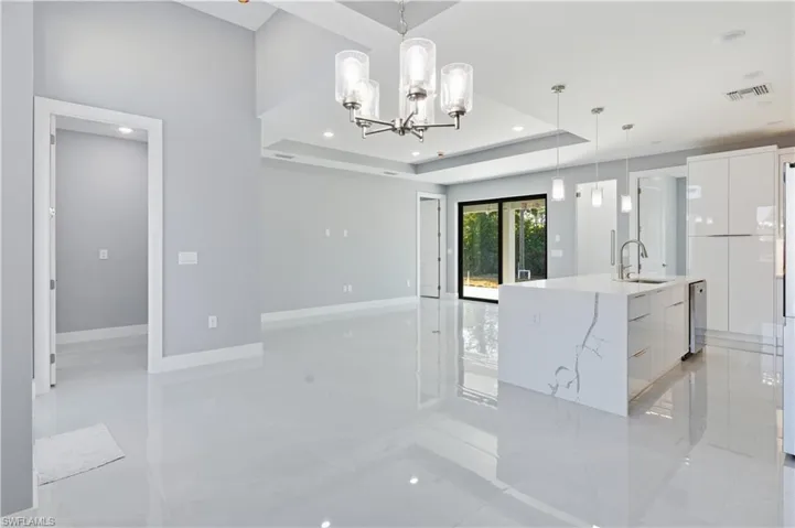 Kitchen featuring modern cabinets, white cabinets, a kitchen island with sink, a chandelier, and a tray ceiling