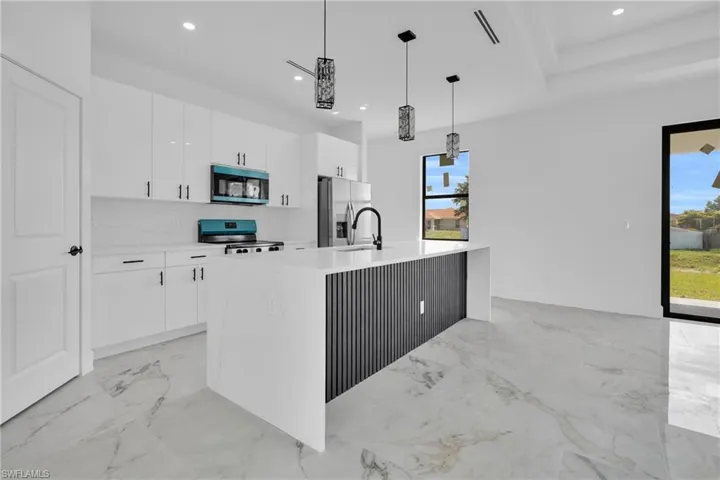 White upper and lower cabinetry, kitchen island with built-in storage, stainless steel appliances, marble-look flooring, and recessed lighting