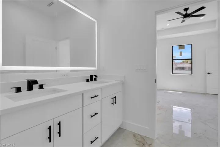Dual vanity with white cabinetry, matte black hardware, and an illuminated rectangular mirror