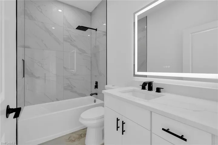 Bathroom featuring a white vanity with integrated sink, a backlit mirror, matte black fixtures, a built-in bathtub, and large format wall tiles