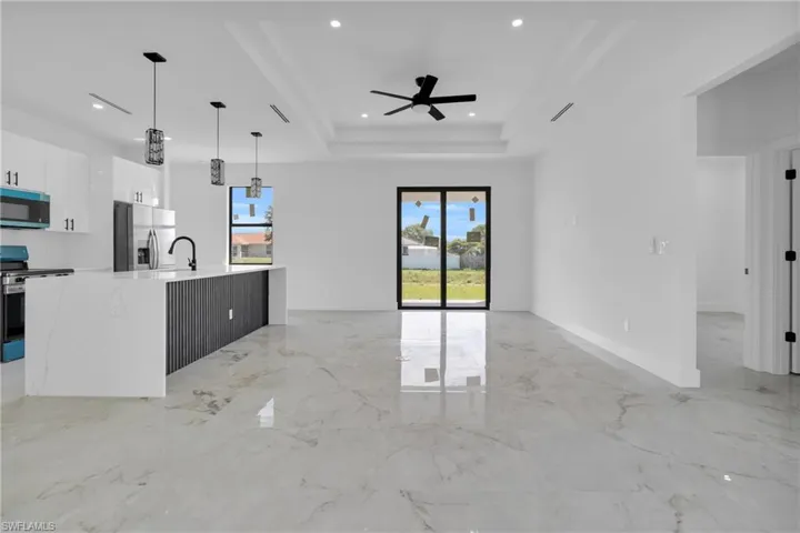 Gleaming large format tile flooring, a contemporary kitchen island with a waterfall countertop, recessed lighting, and a tray ceiling